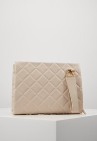 Borsa a tracolla beige trapuntata con una texture liscia e una tracolla removibile. Presenta dettagli in oro e una chiusura con zip sulla parte superiore.