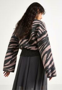 Strikket sweater med et pink og sort zebra mønster, brede ærmer og en mørk ribbet kant. Parret med en flydende sort nederdel.