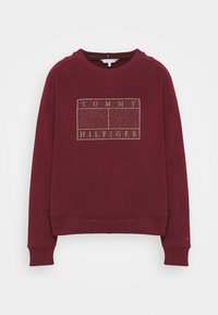 Burgundowy sweter z okrągłym dekoltem, ściągaczami na rękawach i złotym brokatowym logo umieszczonym na środku przodu. Miękka, gładka tekstura materiału.