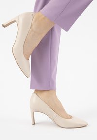 Scarpe con tacco beige a punta arrotondata, in pelle liscia, con un tacco leggermente rialzato; indossate con pantaloni lavanda.
