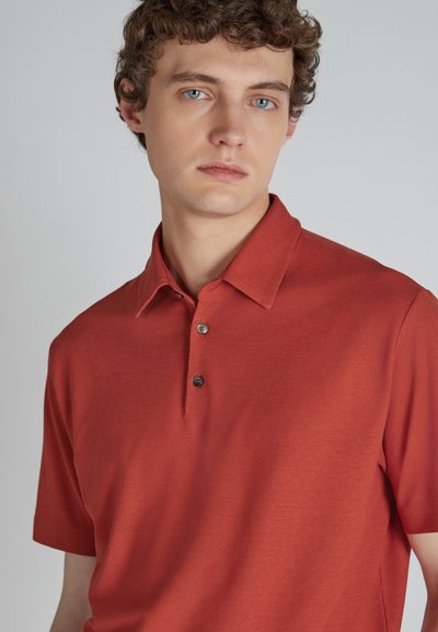 Polo a maniche corte di colore rosso ruggine con colletto, patta con tre bottoni, texture liscia e un sottile motivo melange.