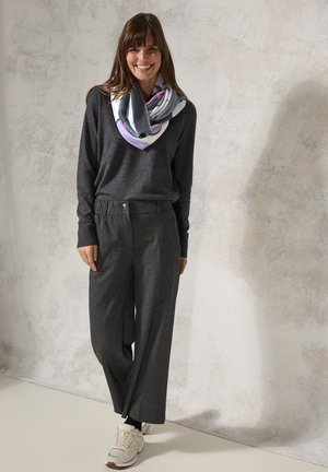 Maglione grigio a maniche lunghe, pantaloni grigi a vita alta e una sciarpa multicolore a fantasia. Il modello si trova su uno sfondo neutro.
