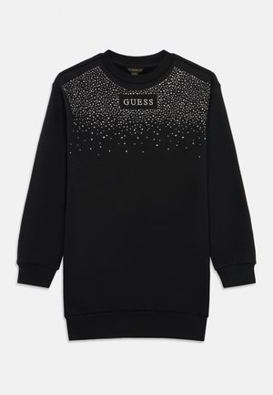 Robe sweat noire à manches longues avec des poignets et un ourlet côtelés, ornée de rivets argentés et du logo "GUESS" sur la poitrine.