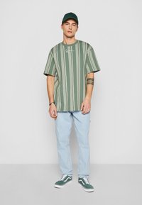 Grönrandig översize t-shirt med en logotyp, matchad med ljusblå jeans och gröna sneakers. Kappen är också grön och matchar t-shirten.