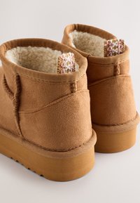 Braune Wildleder-Stiefeletten mit einem weichen Lammfellfutter und einem gewebten dekorativen Akzent am Schaft. Dicke Gummisohlen, runde Zehenform.