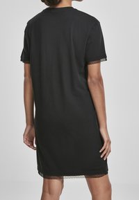 Czarna sukienka T-shirt z krótkimi rękawami, z koronkowym wykończeniem rękawów i dołu. Wykonana z miękkiego materiału o luźnym kroju.