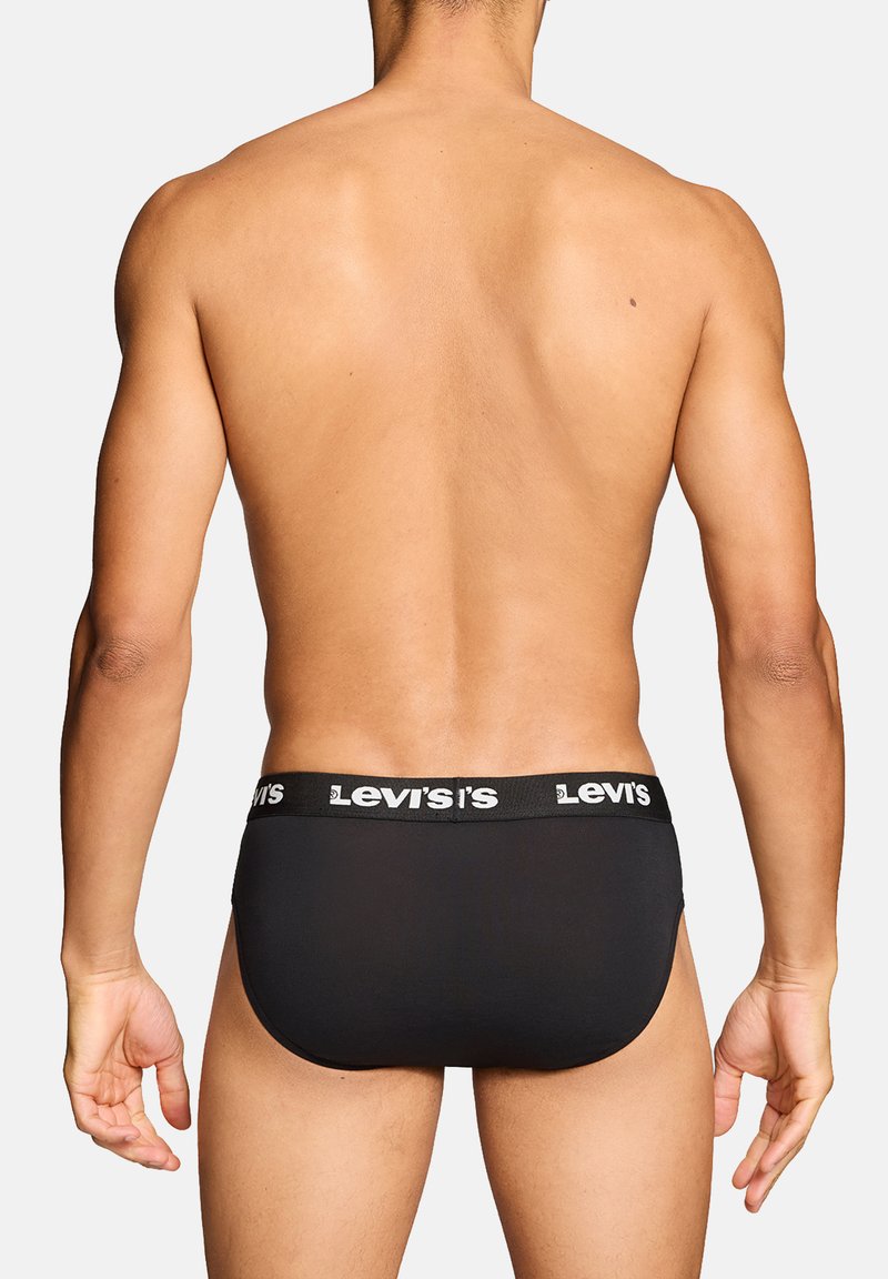 Mann von hinten gesehen, trägt schwarze Levi's Slips mit Logosbund vor hellem, einfarbigem Hintergrund.
