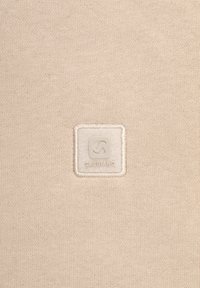 Tessuto beige con texture intrecciata, caratterizzato da una patch quadrata crema in rilievo con la scritta "GABBIANO" e un simbolo logo al centro.