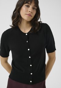 Black short-sleeve cardigan made of knit fabric with a round neckline and front button closure featuring white buttons.