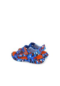 Chanclas coloridas con un patrón geométrico en azul, rojo y blanco, con una superficie texturizada y tiras de velcro para un ajuste seguro.