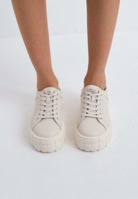Beige leren sneakers met gestructureerde witte rubberen zolen, met een ronde neus, vetersluiting aan de voorkant en een minimalistisch ontwerp.