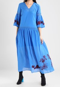 Blauwe katoenen maxi-jurk met een V-hals, uitlopende mouwen en bordeauxrode bloemenborduursels aan de zoom. Lichtgewicht stof met een vloeiende silhouet.