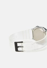 Montre numérique transparente avec un bracelet en silicone transparent, boucle noire et boîtier en ton argenté. L'arrière est lisse et métallique.
