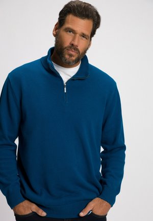Gebreide trui in teal met een halve rits kraag, geribbelde manchet en zoom, gladde textuur en casual pasvorm. Draagt over een wit shirt.