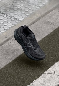 Black athletic shoe with a mesh upper, textured surface, and contrasting dark accents. Features a cushioned sole and lace closure.