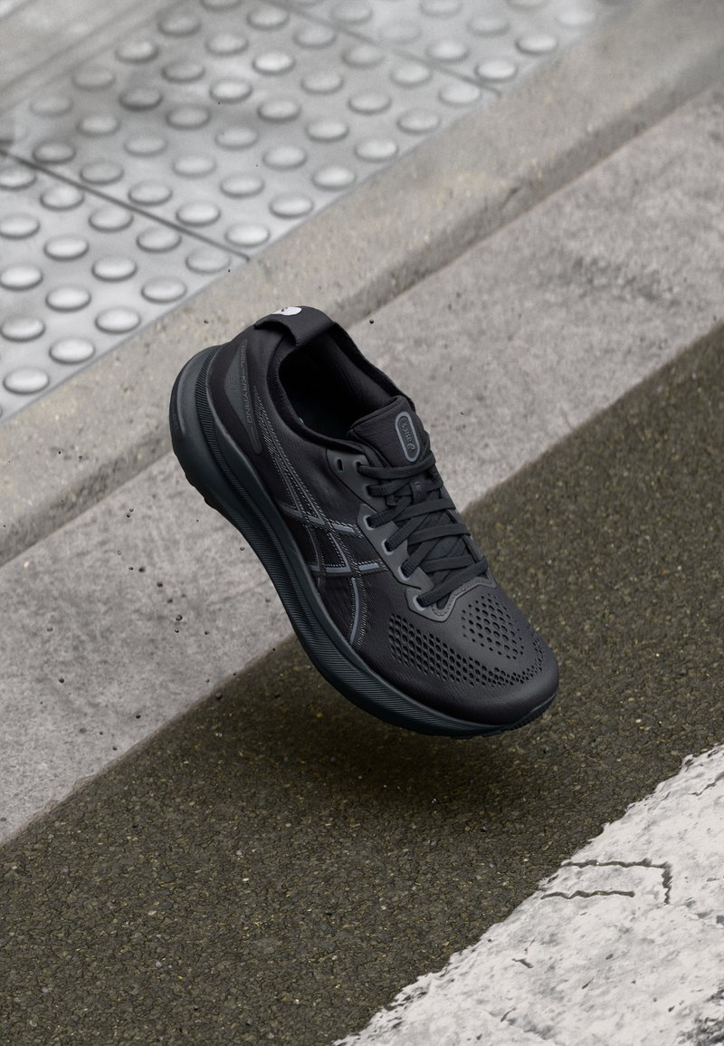 Black athletic shoe with a mesh upper, textured surface, and contrasting dark accents. Features a cushioned sole and lace closure.