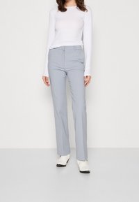 Jasnoszare dopasowane spodnie z prostymi nogawkami, zestawione z obcisłą białą bluzką z długim rękawem. Gładki materiał i brak widocznych wzorów.