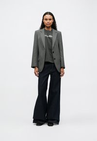 Gray pinstripe tailored blazer, dark gray graphic tee, wide-leg dark denim jeans, black shoes, standing against a plain white background.
