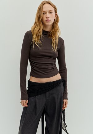 Ruskea pitkähihainen poolopaita, jossa on istuva malli ja sivut rypytettyinä, yhdistetty korkeavyötäröisiin, ohutraitaiseen housuihin ja mustaan teksturoituun kietaisuun.