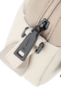 Borsa di stoffa beige con una trama liscia, un tirante nero con un simbolo di avvertimento e cuciture a contrasto lungo i bordi.