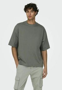 Graues T-Shirt mit kurzen Ärmeln in entspannter Passform und Rundhalsausschnitt. Hergestellt aus weicher Baumwolle, zeichnet sich durch eine glatte Textur und einen geraden Saum aus.