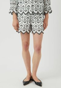 Pantaloni corti bianchi ricamati con motivi floreali neri e bordi scallop, abbinati a ballerine nere a punta.