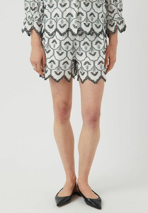 Pantaloni corti bianchi ricamati con motivi floreali neri e bordi scallop, abbinati a ballerine nere a punta.