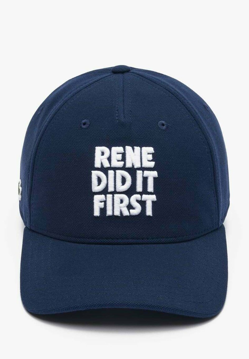 Granatowa czapka baseballowa wykonana z tkaniny, z białym haftowanym napisem "RENE ZROBIŁ TO PIERWSZY." Zakrzywiony daszek, usztywniona korona i regulowany pasek z tyłu.