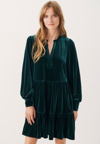 Abito verde in velluto con maniche a sbuffo lunghe, colletto arricciato e gonna a strati. Tessuto liscio e design al ginocchio.