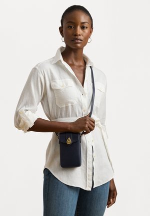 White linen button-up shirt with rolled sleeves, paired with a dark blue crossbody phone pouch featuring gold hardware and a clasp.