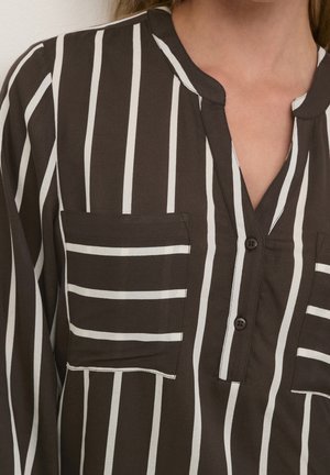 Donkerbruin shirt met verticale witte strepen, twee vierkante borstzakken met horizontale strepen en een gedeeltelijke knoopsluiting bij de hals gedragen door een persoon.