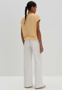 Kurzärmliges, strukturiertes gelbes Oberteil mit lockerer Passform, kombiniert mit weißen weit geschnittenen Hosen. Minimalistisches Design mit einem sanften, lässigen Look.