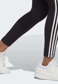 Sorte træningsleggings har hvide lodrette striber langs siderne og bæres med hvide sneakers, der har mesh og solide såler.