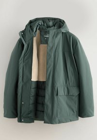 Grüne isolierte Jacke mit einem weichen beigen Innenfutter, einer Kapuze und mehreren Taschen. Verfügt über eine glatte Außentextur und Druckknopfverschlüsse.