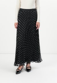 Gonna nera a pieghe con pois bianchi, dotata di una cintura elastica. Indossata con un top bianco a coste e scarpe nere con punta.