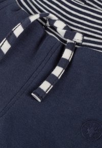 Nahaufnahme von navyblauen Hosen mit gestreiftem Kordelzug und Bund, die die Stoffstruktur und das gestickte kreisförmige Logo zeigen.