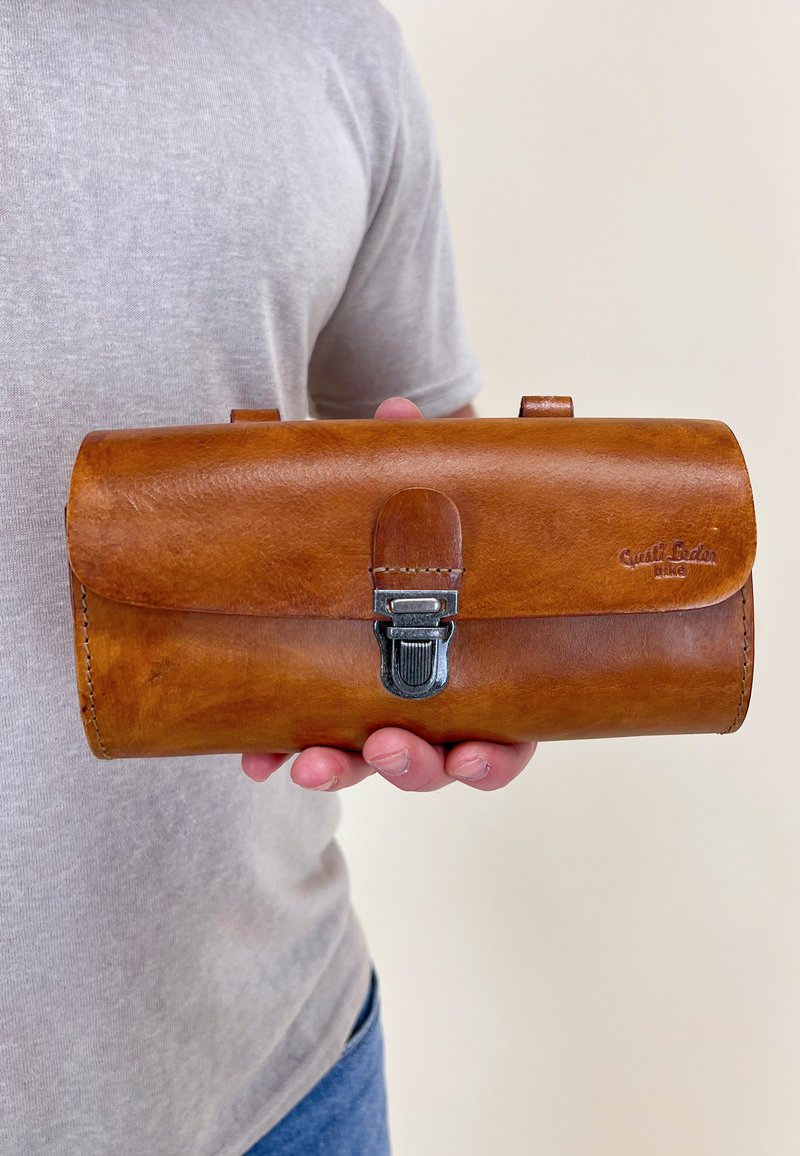Brown leather wallet with a rounded flap, silver buckle closure, and embossed logo. Features smooth texture and minimalistic design.