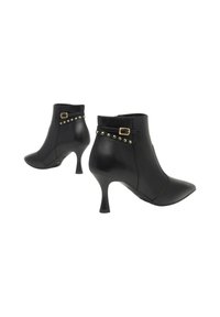 Stivaletti in pelle nera con punta affusolata, tacchi alti sottili e cinghie decorative con borchie dorate e fibbie intorno alla caviglia.