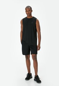 Svart ärmlös träningslinne och shorts, båda gjorda av lättviktsmaterial. Linnen har en liten logotyp; skorna är svarta och med textur.