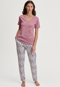 Roze V-hals shirt gecombineerd met witte broek met patroon, voorzien van bloemmotieven in roze, blauw en groen. Zachte stof; comfortabele pasvorm.