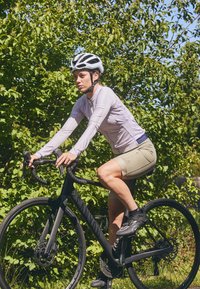 Cycling outfit featuring a long-sleeve light purple top and light green shorts; rider on a matte black bike with black wheels and handles.