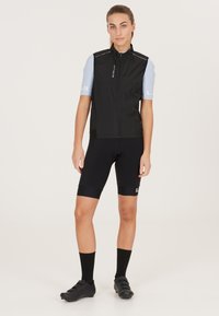 Schwarze Radweste mit hohem Kragen, kombiniert mit schwarzen Shorts. Hellblaue Kurzarm-Shirts mit reflektierenden Details und sportlicher Passform.