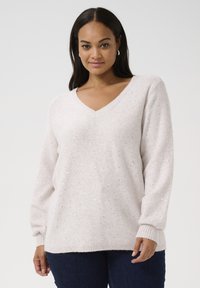 Pulover bej deschis din tricot moale, cu decolteu în V, având puncte metalice dispersate, mâneci lungi și manșete cu costuri.