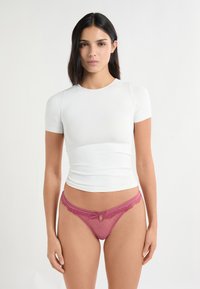 Top bianco aderente a maniche corte in tessuto liscio, abbinato a slip di pizzo lampone con fiocco e motivo a pois.