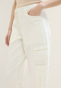 Witte cargobroek van katoen met een gladde textuur, voorzien van meerdere cargopockets en een knoopsluiting bij de taille.