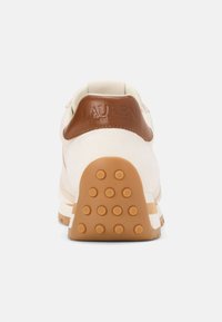 Kremowe sneakersy z brązowym skórzanym akcentem na pięcie, teksturowaną gumową podeszwą z okrągłymi wypustkami oraz wytłoczonym logo na pięcie.