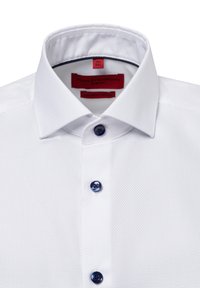 Weißes Slim-Fit-Hemd mit strukturiertem Stoff, einem starren Kragen und drei dunkelblauen Knöpfen an der Knopfleiste. Rotes Etikett im Kragen.