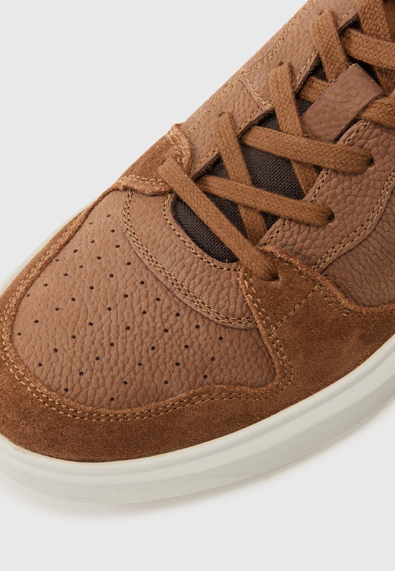 Brauner Sneaker aus strukturiertem Leder und Wildleder, mit Perforationen an der Zehenpartie, braunen Schnürsenkeln und einer weißen Gummisohle.