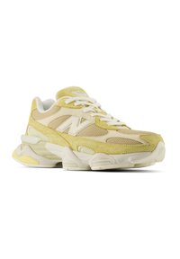 Baskets de sport beige et jaune clair avec lacets blancs, empiècements en mesh et en daim, semelle épaisse et un logo "N" bien visible sur le côté.