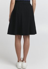 Zwarte knie-lange rok met gathered taille, van een katoenmixstof en een soepele textuur, gecombineerd met witte sneakers.